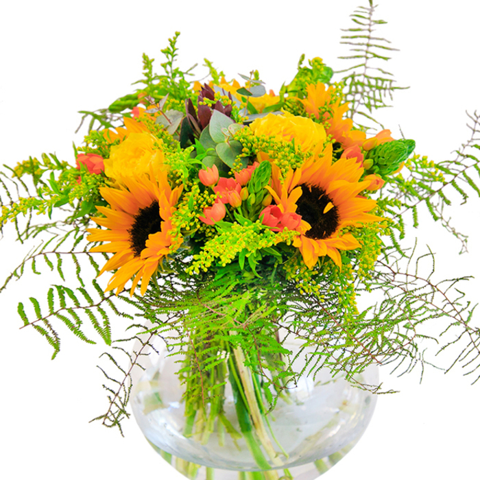 This vibrant, sun-drenched arrangement immediately conjures feelings of celebration and joy, much like a festival morning on Totteridge Green. Showcasing striking sunflowers-each a burst of luminous yellow-orange petals surrounding deep, chocolate-brown centres-they form a radiant backdrop for delicately spiralled yellow roses, whose tightly layered blooms recall antique charm and careful craftsmanship. Red hypericum berries cluster among the flowers, their gleaming surfaces contrasting deliciously with the soft, matte petals and bringing energy reminiscent of a bustling Saturday at the Totteridge market. Wisps of verdant fern and textured greenery create a relaxed, natural cascade, echoing the movement of tree branches along the Dollis Valley. Misty eucalyptus and tiny yellow filler blossoms (possibly solidago) add subtle colour complexity, enhancing the rustic appeal. The round, crystal-clear glass vase cradles the bouquet, its water amplifying the garden-fresh stems-a pure, refreshing detail that underscores the arrangement's vitality. Inhaling the gentle scent, one senses late summer fields on the village edge as sunlight glances through open windows. Whether as a memorable birthday gesture, anniversary tribute, or a simple act of kindness, this floral design embodies the abundant beauty and warmth of the Totteridge community, crafted with the soulful expertise that defines Flowers Totteridge.