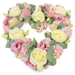 A pastel heart-shaped wreath is displayed against a spotless white background, its soft colours and rich textures creating an atmosphere of peace and remembrance reminiscent of a quiet walk through Totteridge's tree-lined streets. The heart is completely filled with flowers, giving it a plush, luxurious appearance with no gaps or harsh edges. Creamy ivory and pale yellow roses form the visual anchors, their velvety petals spiralling inward in perfect rosettes that speak of elegance and devotion. Between them, light pink carnations are packed closely together, each bloom with finely frilled petals that overlap like gentle waves, adding a comforting, almost cloud-like softness. Interspersed through this pastel base are deeper tones of mauve and magenta-pink lisianthus, their slightly more open, trumpet-shaped flowers and subtle tonal shifts lending depth and a sense of quiet, dignified grace. Sprays of tiny yellow-green buds peek from between the petals, suggesting freshness and continuity, while slim stems of silvery-green eucalyptus weave through the arrangement. The eucalyptus leaves, round and softly matte, trace the curves of the heart and cool the colour palette, balancing the sweetness of the pinks and creams. The overall composition feels calm, compassionate, and deeply personal - a floral tribute that might rest beside a casket or memorial frame at a funeral service in Totteridge. It conveys sympathy, gratitude, and enduring love, offering visual comfort to family and friends gathered to say goodbye, and reflecting the thoughtful work of a skilled local florist devoted to honouring each life with care.